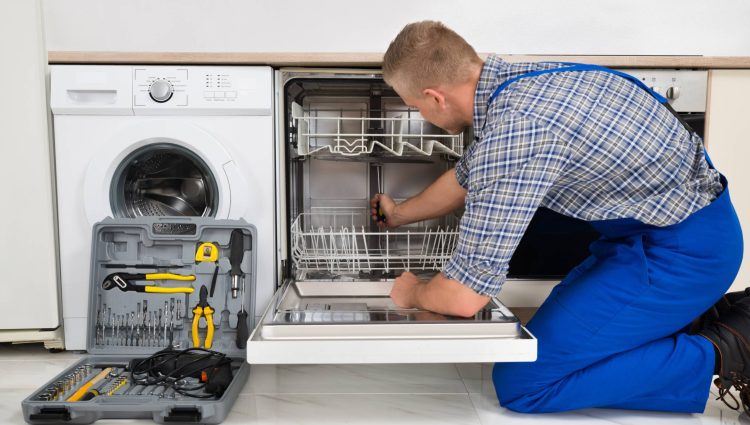 Young Man In Overall With Toolbox Repairing Dishwasher